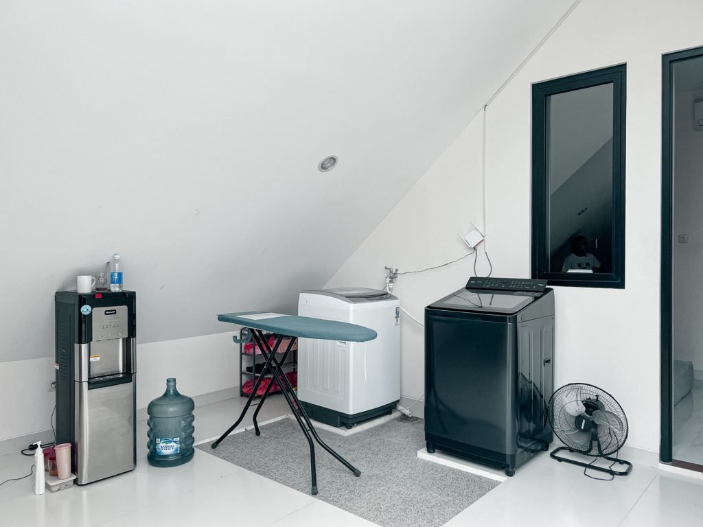 The shared laundry room at Arcelon Premiere with a washing machine, water dispenser and ironing board