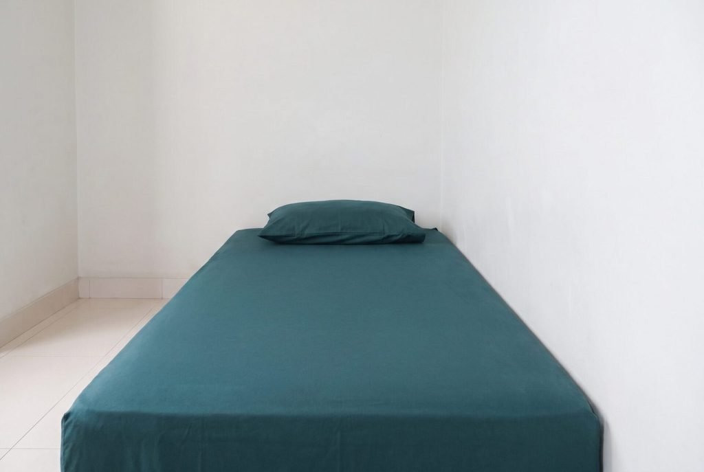 A made single bed against a plain wall in a room at Arcelon Stay Karawaci