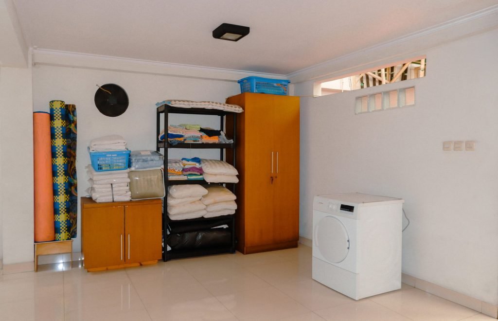 The laundry room at Arcelon Stay Karawaci with a washing machine, shelving and folded linen