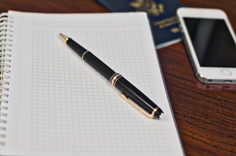 A passport, notebook and pen laid out on a wooden desk