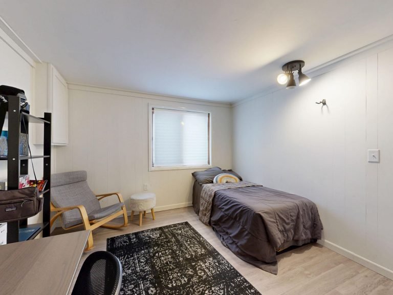 A small furnished room with a single bed, armchair and plain decor
