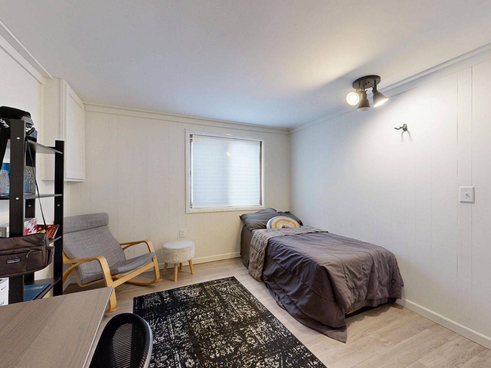 A small furnished room with a single bed, armchair and plain decor