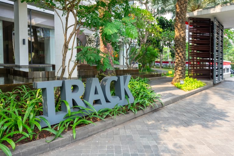 Sculptural TRACK sign at the entrance to the running track, set among planting