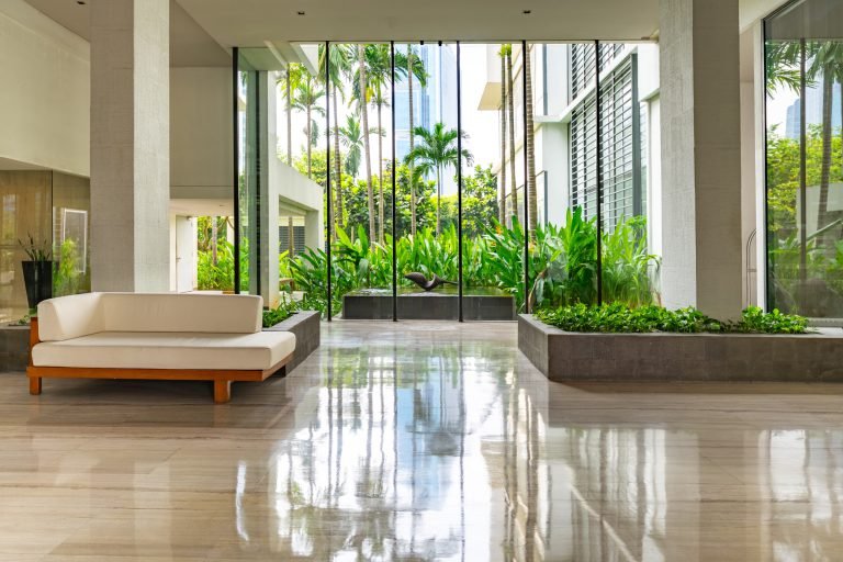 Lobby lounge with a daybed facing a full-height glass wall onto a planted courtyard, polished stone floor throughout