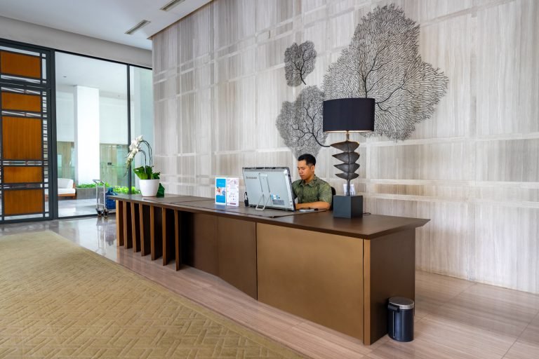 Reception desk in dark timber and stone, with coral-motif wall art and a concierge on duty
