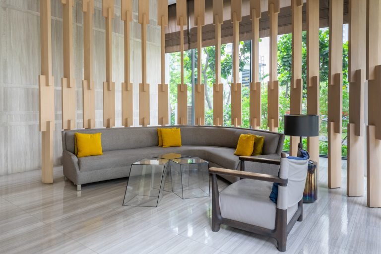 Seating nook with a curved grey sofa, yellow cushions and armchairs behind timber screening