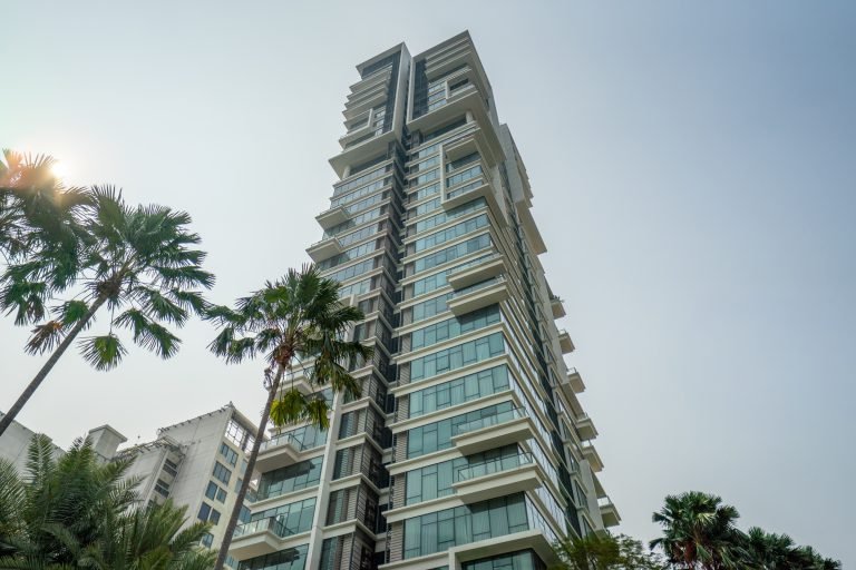 Exterior of the residential tower seen from the garden, framed by palm trees against a bright sky