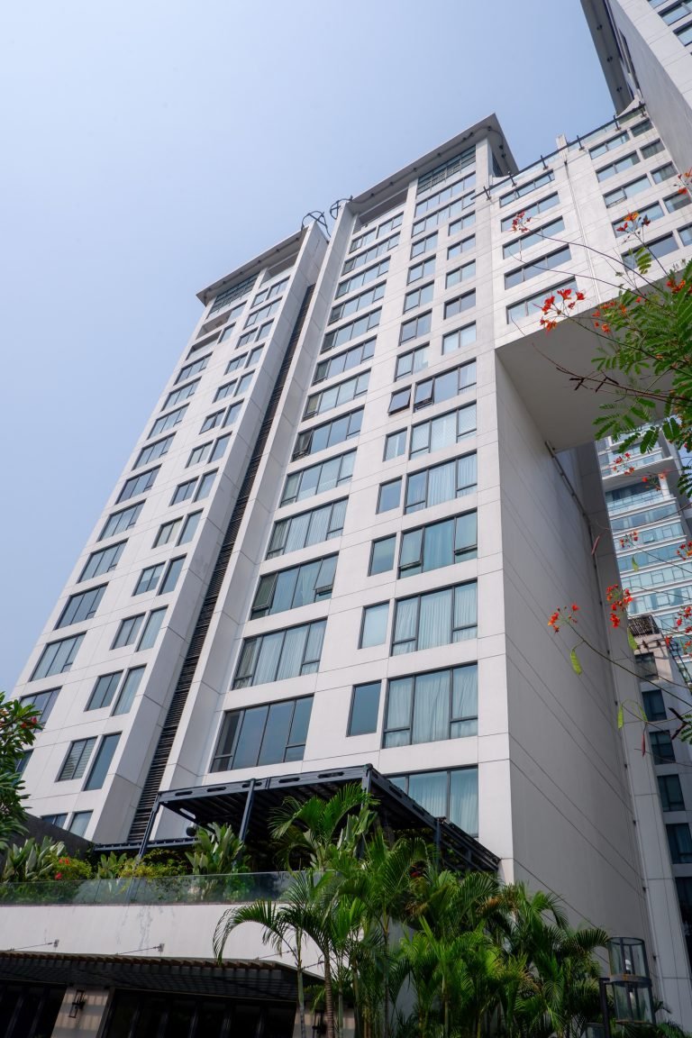 Full-height view of the tower façade with balconies, surrounded by mature planting