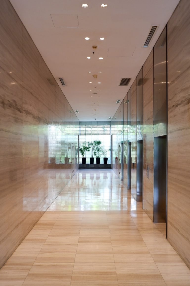 Lift lobby corridor in pale marble, looking through to the daylit entrance beyond