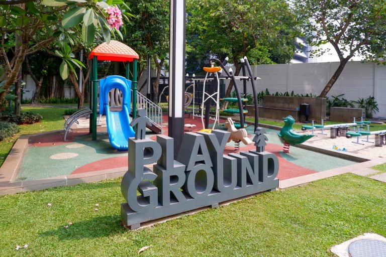 Children's playground with a slide, climbing frame and a large sculptural PLAYGROUND sign on soft rubber matting