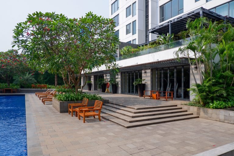 Wide view of the pool deck with loungers, steps down to the water and the residential tower behind