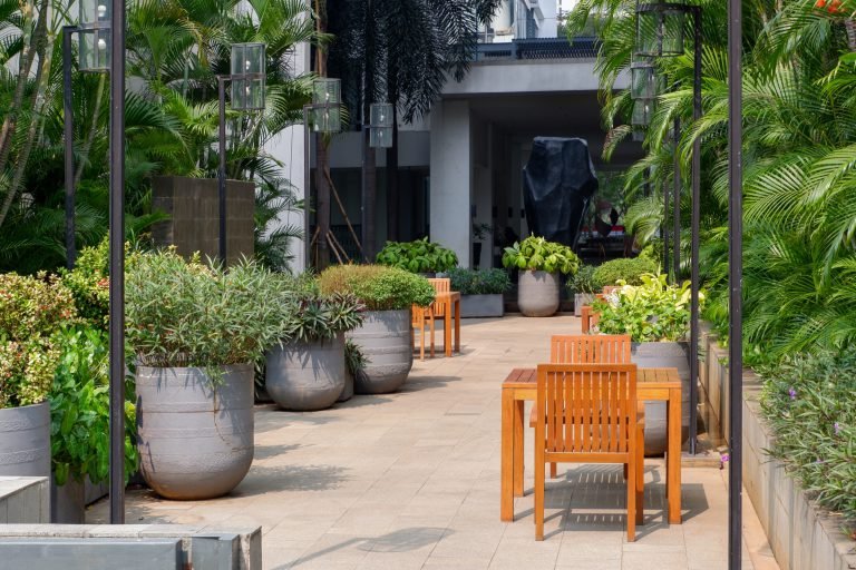 Paved courtyard beside the pool with large planters, timber armchairs and a lounge seating group