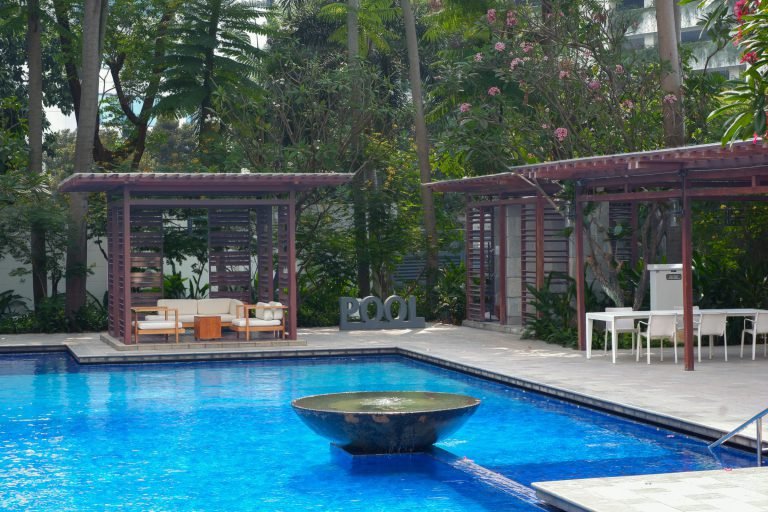 Pool with a stone water feature at one end and a shaded pavilion with seating alongside
