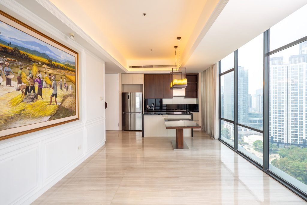 Open-plan living and dining area leading to the kitchen, framed artwork on the left and a wall of city-facing windows