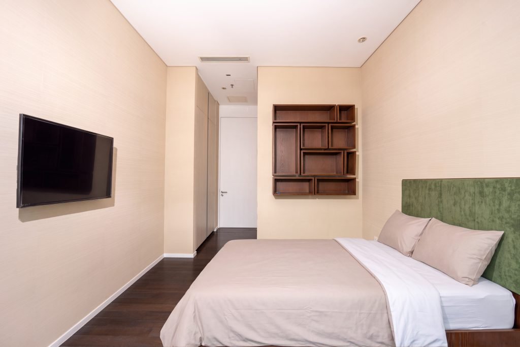 Bedroom with wall-mounted TV opposite the bed and open timber display shelving beside the wardrobe