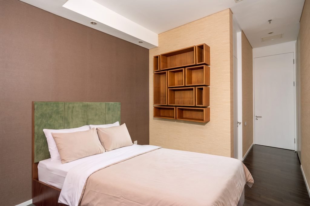 Bedroom corner showing the green headboard against a taupe wall and a geometric timber shelf unit