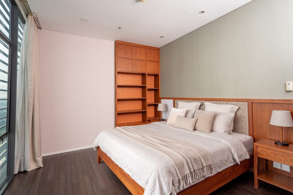 Bedroom with a timber bookshelf headboard wall, bedside lamps and sheer curtains over the window
