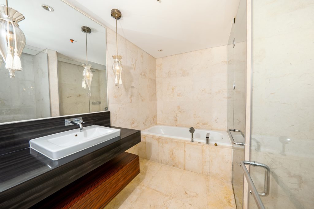 Marble bathroom with a vessel basin on a dark wood vanity, pendant lights and a glass-enclosed bathtub