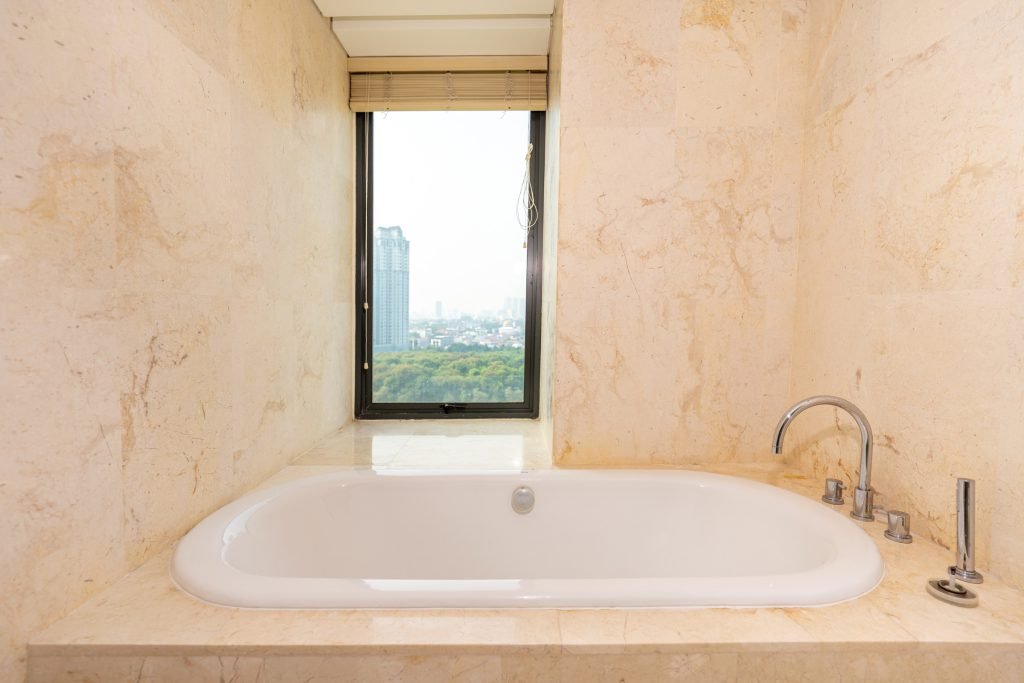 Bathtub set beneath a window with a daytime view over the city