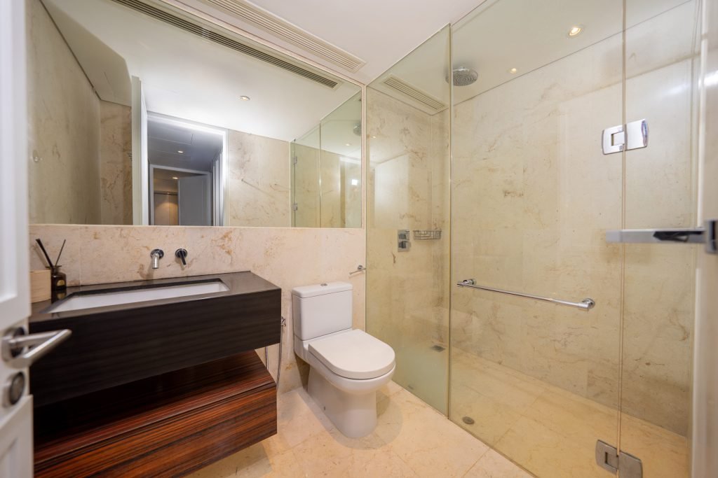 Marble bathroom with dark stone basin, wall mirror and glass shower screen beside the toilet