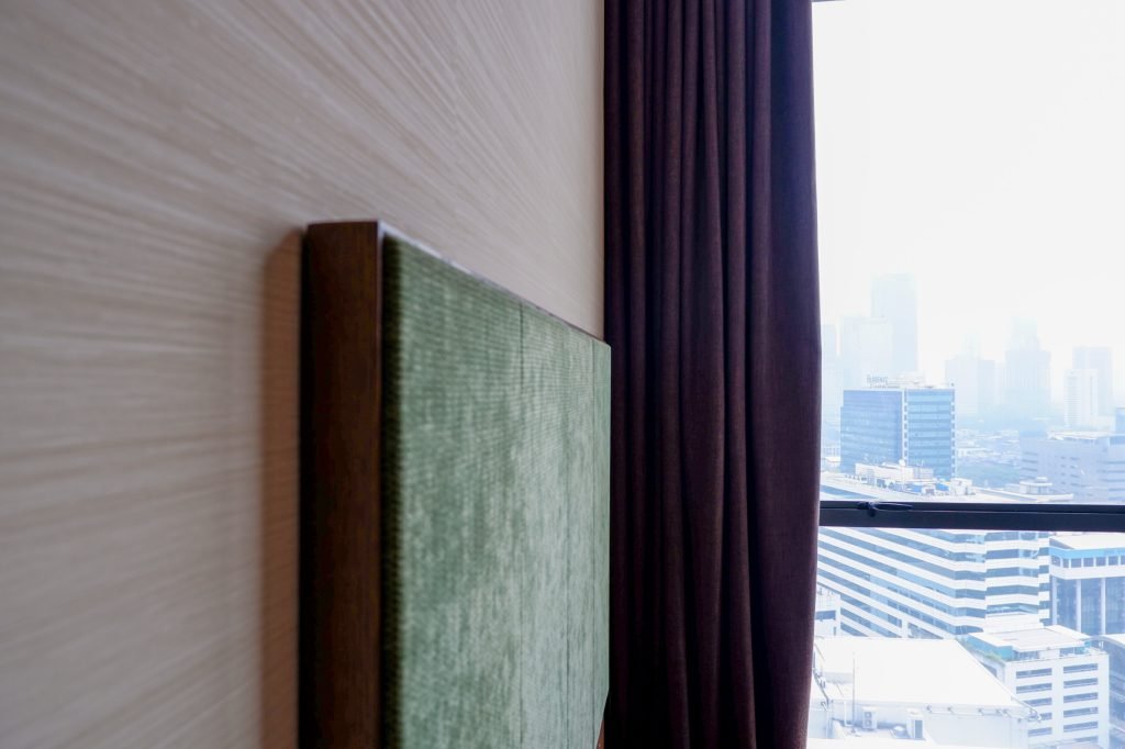 Detail of the green upholstered headboard against the window, city skyline beyond