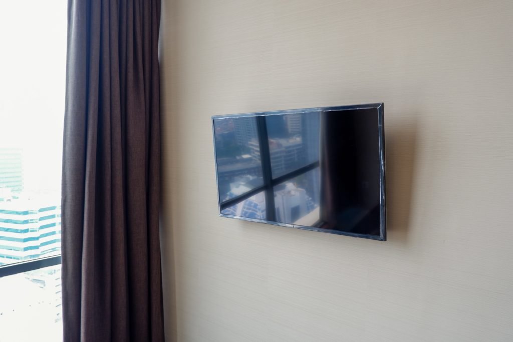 Wall-mounted flat-screen TV beside a curtained window with a city view