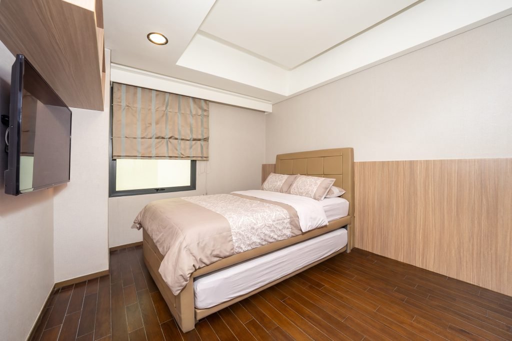 Bedroom with wall-mounted TV, timber panelling and a roller blind over the window