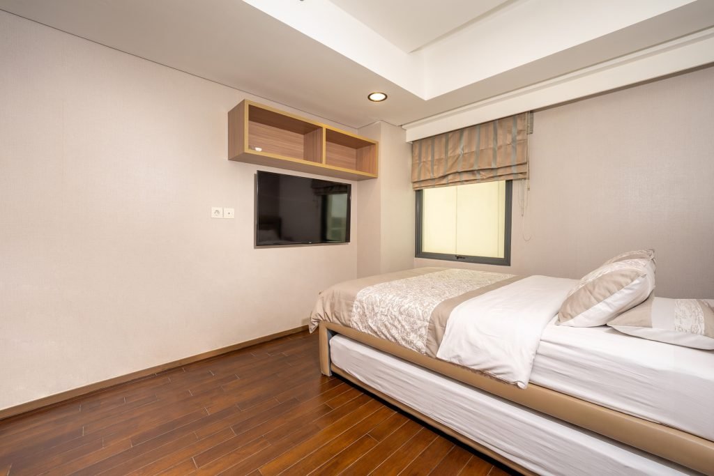 Bedroom with a wall-mounted TV, overhead cabinet and a window looking onto the street