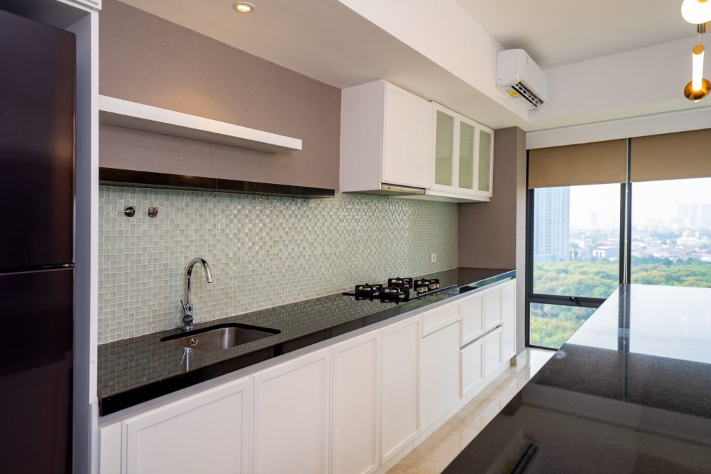 Kitchen with white cabinetry, mosaic tiled splashback, granite worktop and a city view beyond the glass door