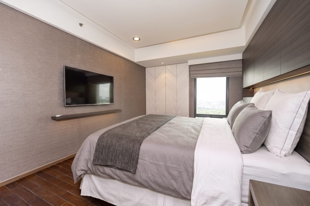 Bedroom with wall-mounted TV, timber headboard wall and a window with a city outlook